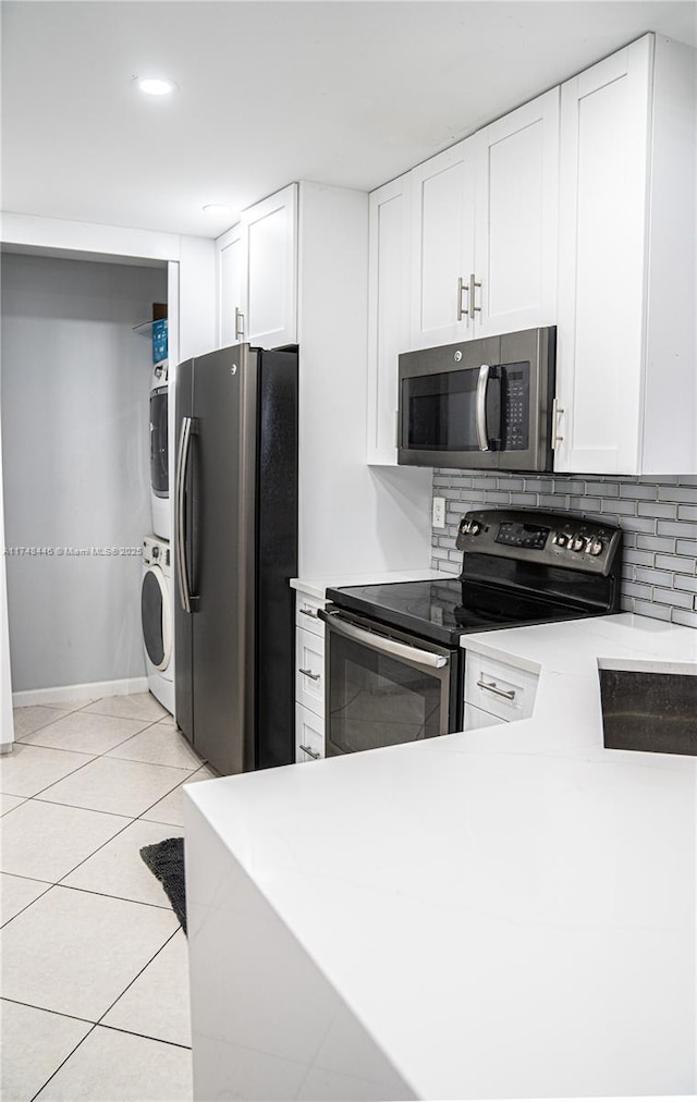 kitchen featuring stainless steel appliances, light countertops, stacked washer and clothes dryer, and white cabinets