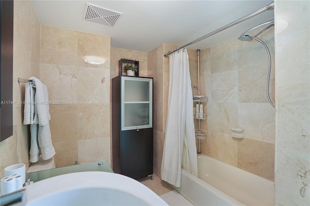 bathroom featuring shower / bath combo, visible vents, and tile walls