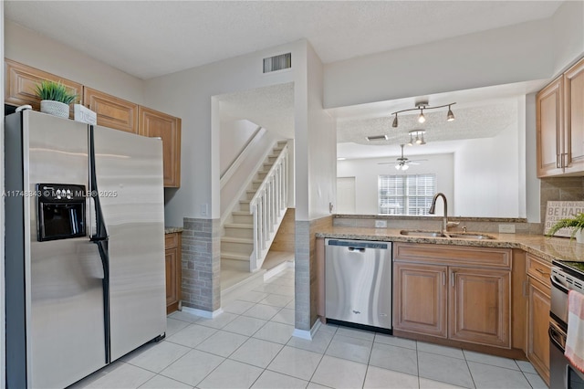 kitchen with light tile patterned floors, a textured ceiling, a sink, appliances with stainless steel finishes, and light stone countertops