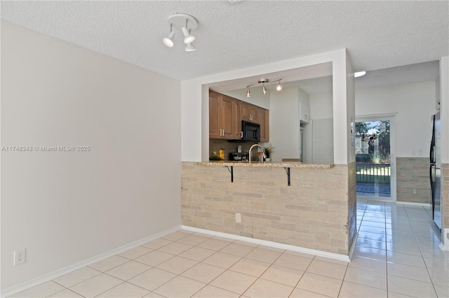 kitchen featuring light tile patterned floors, brown cabinetry, a sink, black microwave, and a peninsula