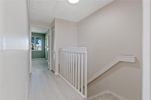 hall with light wood finished floors, attic access, and baseboards