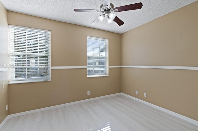 spare room with a ceiling fan, light wood-style flooring, baseboards, and a textured ceiling