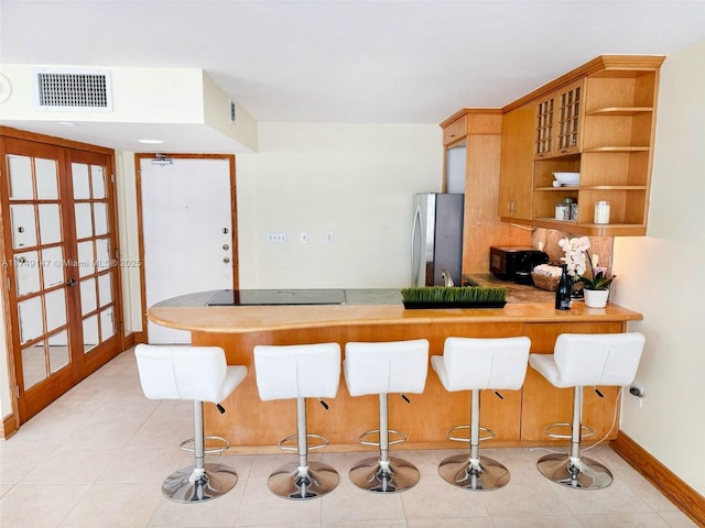 kitchen with open shelves, visible vents, freestanding refrigerator, a kitchen bar, and black electric cooktop