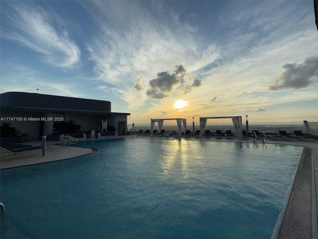 pool at dusk featuring a water view and a community pool