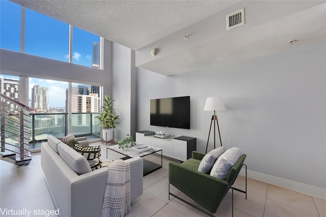 living area featuring a textured ceiling, light tile patterned floors, visible vents, baseboards, and stairs