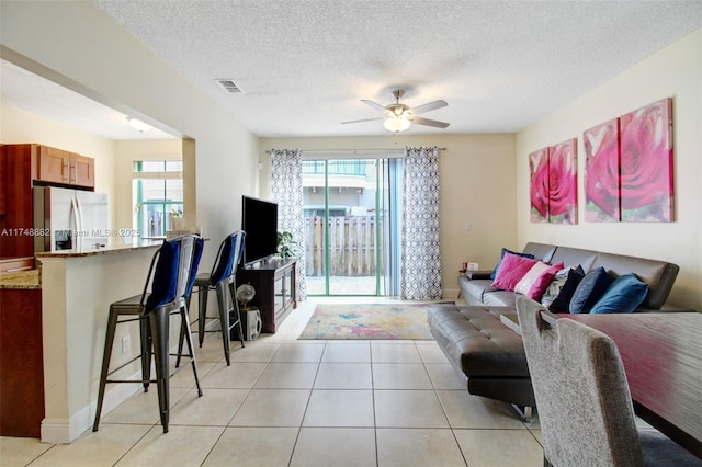 living area featuring visible vents, ceiling fan, a textured ceiling, and light tile patterned floors