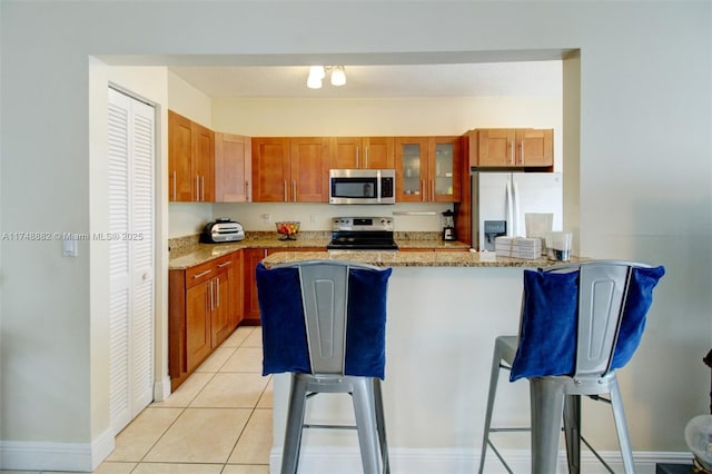 kitchen with stainless steel appliances, a breakfast bar, glass insert cabinets, and light stone counters