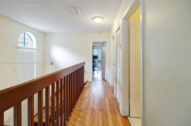 corridor featuring an upstairs landing, visible vents, light wood-style flooring, and a textured ceiling