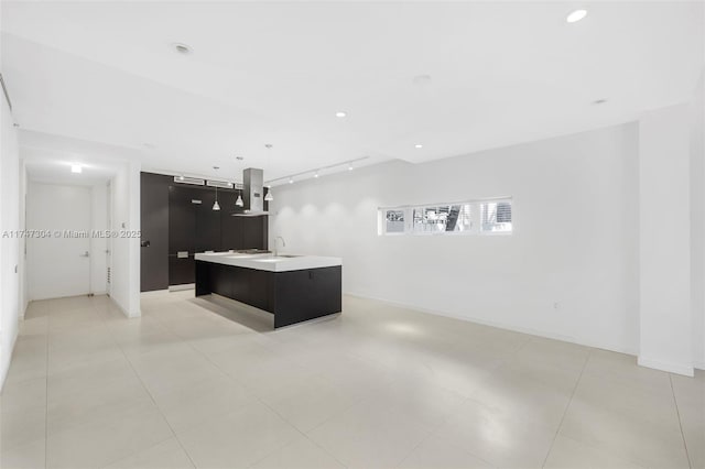 kitchen featuring pendant lighting, light countertops, a kitchen island with sink, wall chimney range hood, and modern cabinets