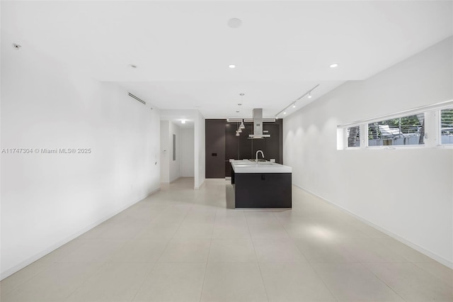 kitchen featuring open floor plan, light countertops, range hood, an island with sink, and track lighting