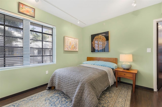 bedroom featuring rail lighting, baseboards, and dark wood-style flooring