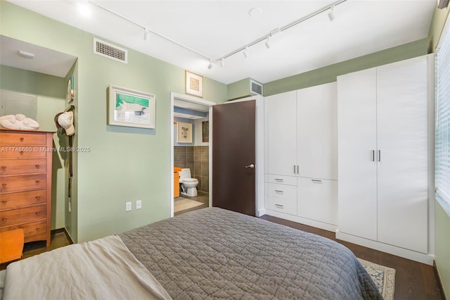 bedroom with ensuite bathroom, dark wood-style floors, visible vents, and track lighting