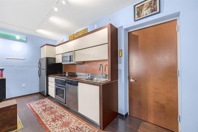 kitchen featuring appliances with stainless steel finishes, white cabinetry, a sink, and dark wood-type flooring