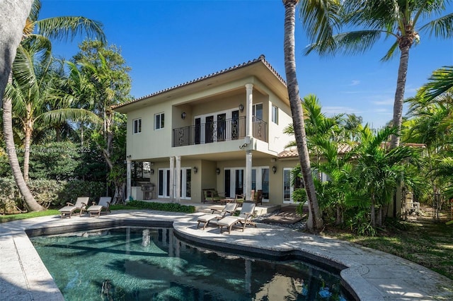 rear view of house with an outdoor pool, french doors, a patio, and a balcony