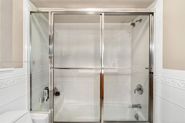 bathroom featuring tile walls, toilet, and bath / shower combo with glass door