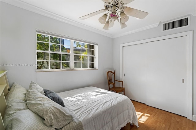 bedroom featuring a closet, visible vents, ornamental molding, a ceiling fan, and wood finished floors