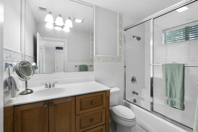 bathroom featuring visible vents, toilet, shower / bath combination with glass door, vanity, and tile walls