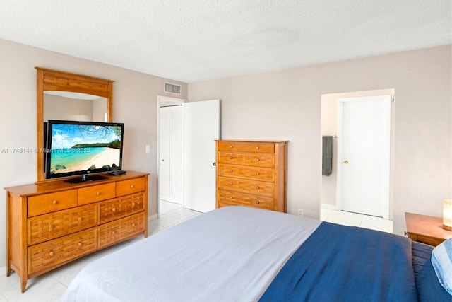 bedroom featuring light tile patterned flooring, a textured ceiling, visible vents, and connected bathroom