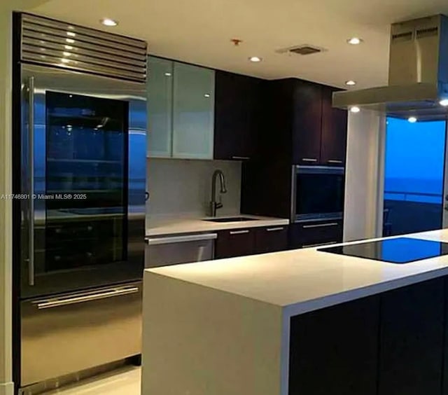 kitchen featuring a kitchen island, range hood, black electric cooktop, light countertops, and a sink