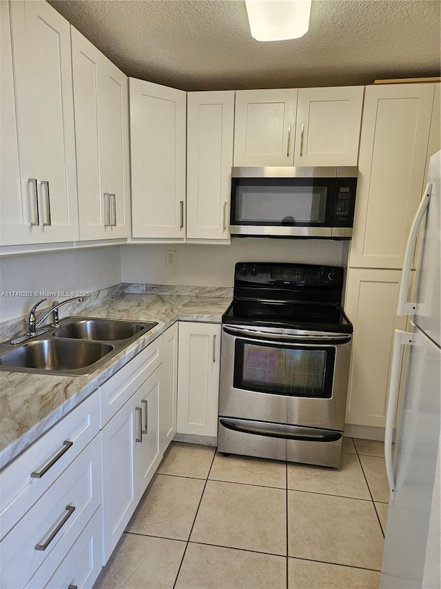 kitchen featuring light tile patterned floors, appliances with stainless steel finishes, white cabinetry, a sink, and light stone countertops