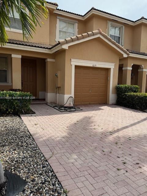 multi unit property with a garage, a tile roof, decorative driveway, and stucco siding