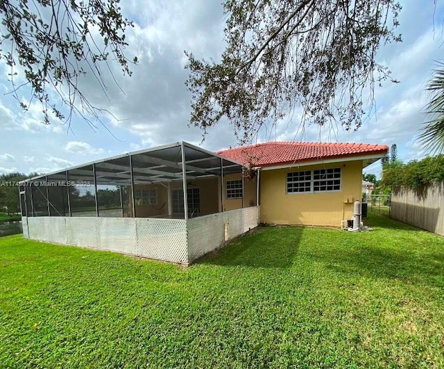 rear view of house featuring a tile roof, stucco siding, a lawn, glass enclosure, and fence