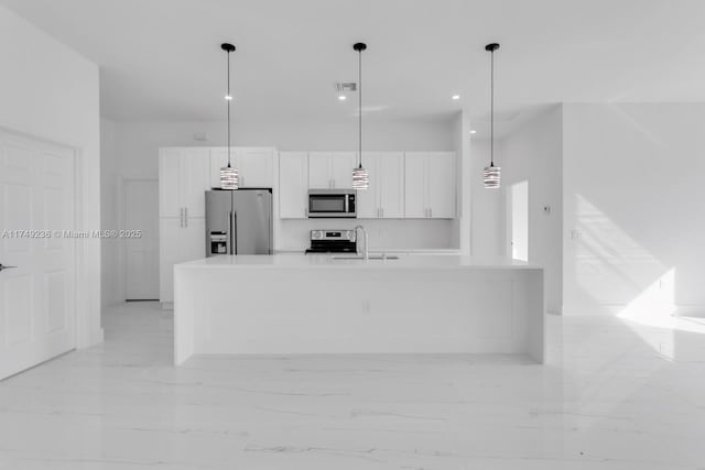 kitchen with an island with sink, hanging light fixtures, stainless steel appliances, light countertops, and white cabinetry