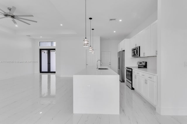 kitchen with a center island with sink, stainless steel appliances, light countertops, hanging light fixtures, and a sink