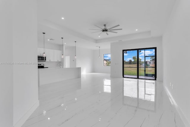 unfurnished living room featuring recessed lighting, a sink, a ceiling fan, baseboards, and a raised ceiling