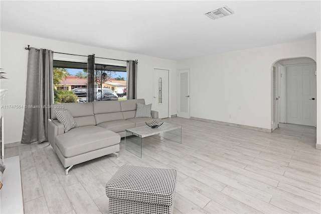 living area with light wood-type flooring, baseboards, visible vents, and arched walkways