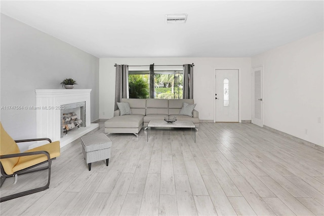 living area with light wood finished floors, baseboards, visible vents, and a fireplace with raised hearth