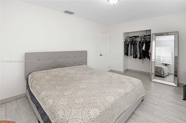 bedroom with light wood finished floors, baseboards, visible vents, and a closet