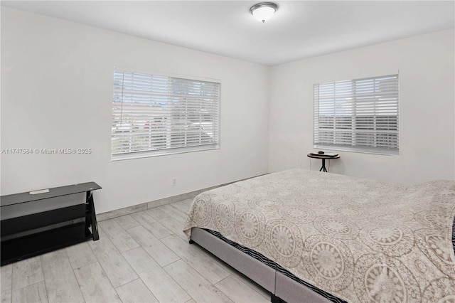 bedroom with light wood-style floors, multiple windows, and baseboards