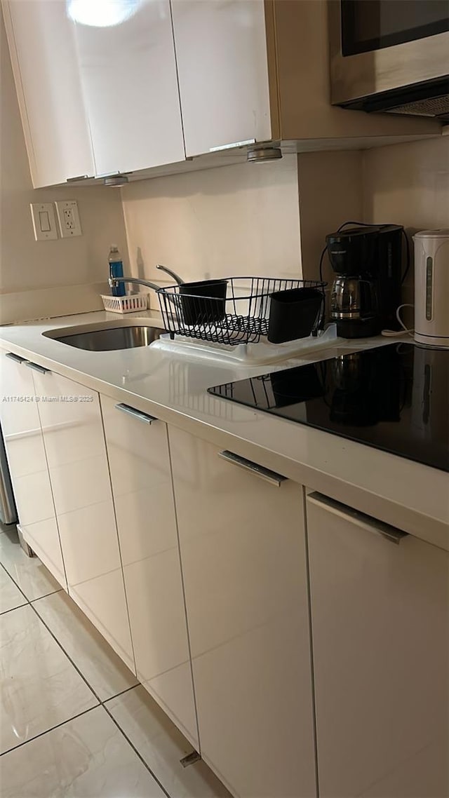 kitchen featuring white cabinets, light countertops, stainless steel microwave, and black electric cooktop