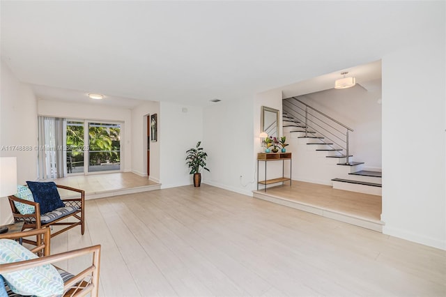 living area with light wood-style flooring, stairs, and baseboards