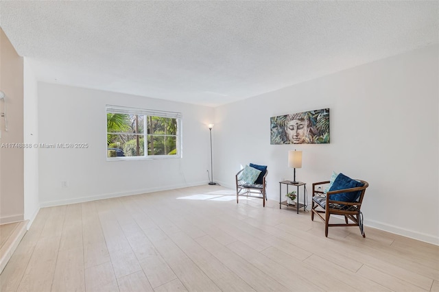 living area featuring a textured ceiling, light wood-type flooring, and baseboards