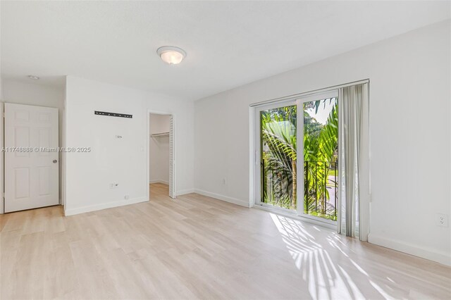 unfurnished bedroom featuring baseboards, light wood finished floors, a walk in closet, and access to exterior