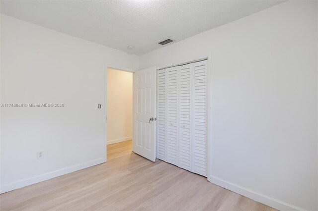 unfurnished bedroom featuring light wood-style flooring, a closet, visible vents, and baseboards