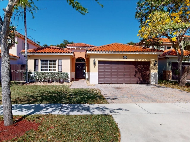 mediterranean / spanish-style home featuring a garage, a tile roof, fence, decorative driveway, and stucco siding