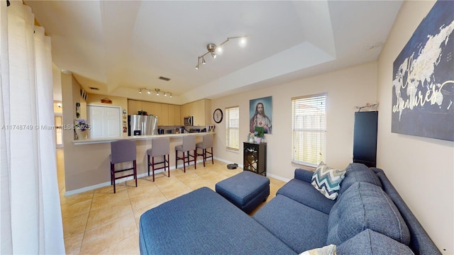 living room with rail lighting, baseboards, a tray ceiling, and light tile patterned flooring