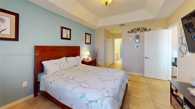bedroom featuring a tray ceiling, visible vents, ensuite bathroom, light tile patterned flooring, and baseboards