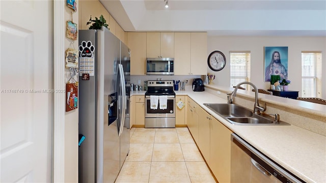 kitchen with light tile patterned floors, cream cabinets, stainless steel appliances, light countertops, and a sink