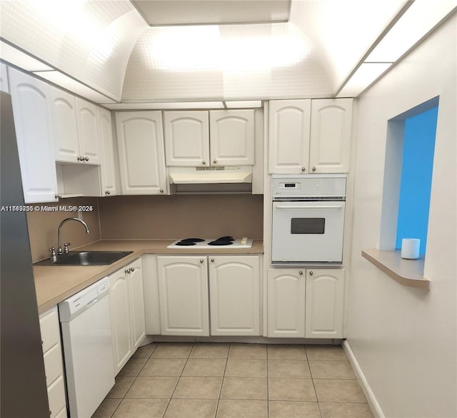 kitchen with light tile patterned floors, under cabinet range hood, white appliances, a sink, and white cabinets