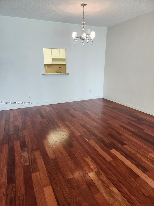 empty room with baseboards, dark wood finished floors, a textured ceiling, a chandelier, and a sink