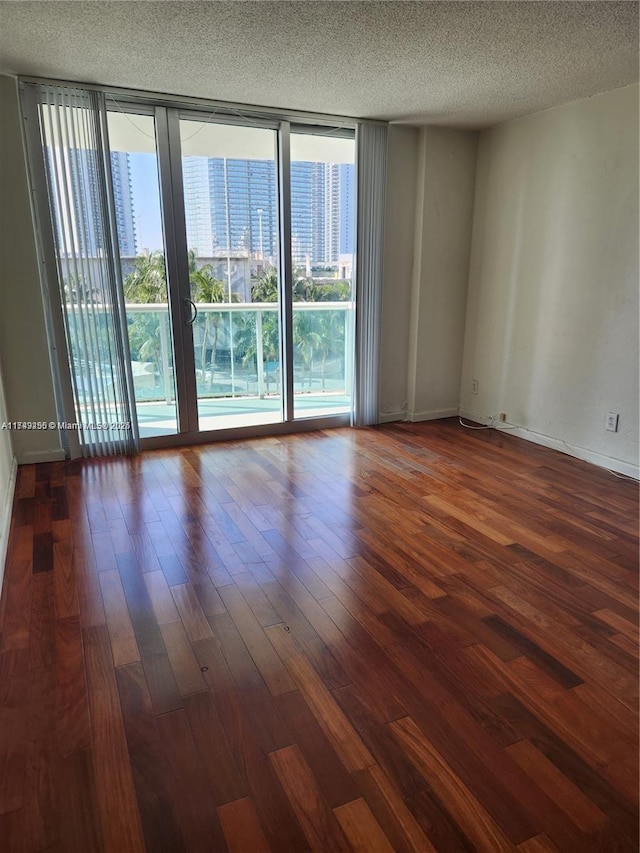 spare room with expansive windows, a textured ceiling, dark wood finished floors, and a city view