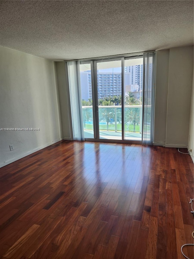 unfurnished room with dark wood-style floors, a view of city, floor to ceiling windows, and a textured ceiling