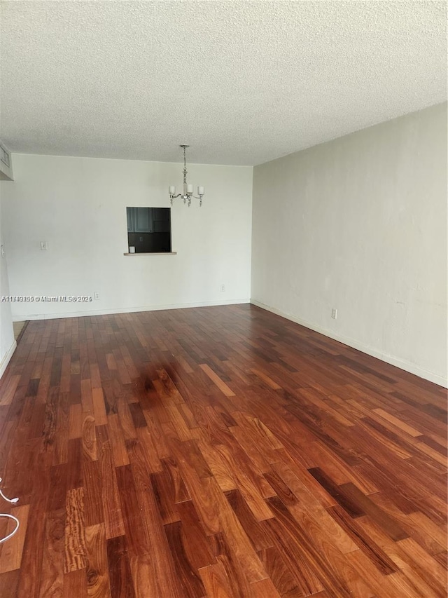 unfurnished room featuring a textured ceiling, a notable chandelier, and wood finished floors