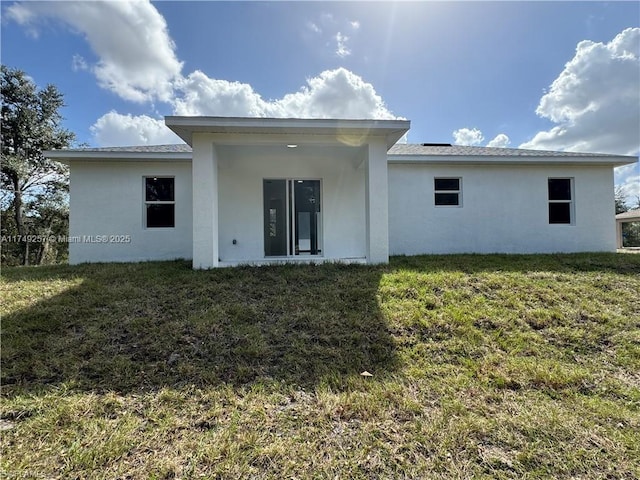 rear view of house featuring a yard and stucco siding