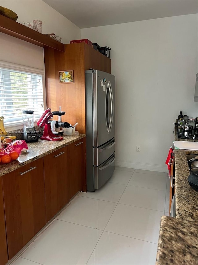 kitchen featuring light stone countertops, light tile patterned floors, baseboards, and freestanding refrigerator