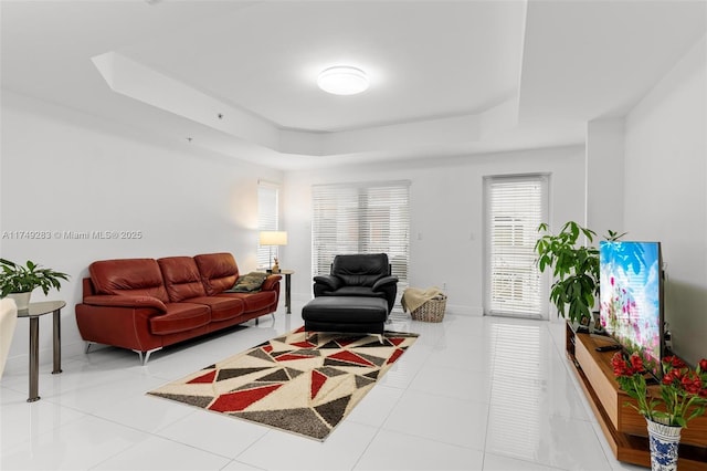 living room with tile patterned flooring, a raised ceiling, and baseboards
